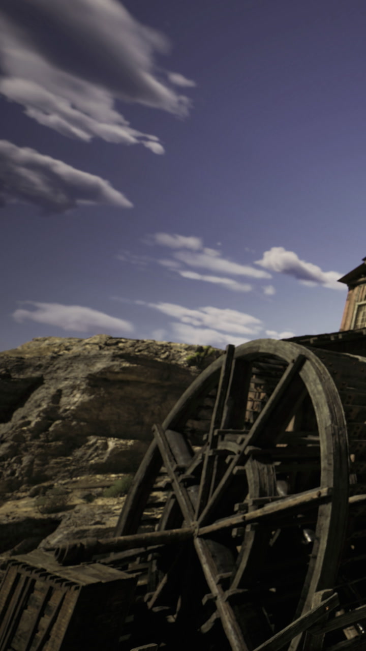 Water wheel turning gently under a bright sky near rugged cliffs
