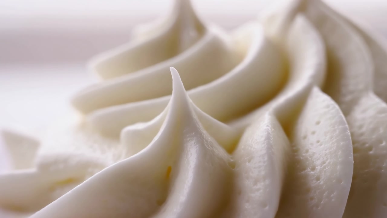 Close-up de espiral de cobertura de creme de manteiga branca, pico feito com bico de confeitar no bolo, iluminação de estúdio com fundo neutro suave.