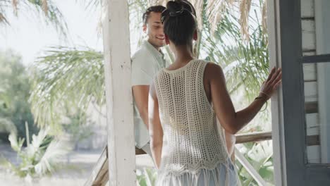 happy diverse couple talking and embracing on sunny beach house porch, in slow motion