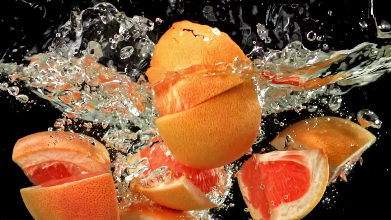 Sakte film av friske grapefruktskiver som plasker ned i vann