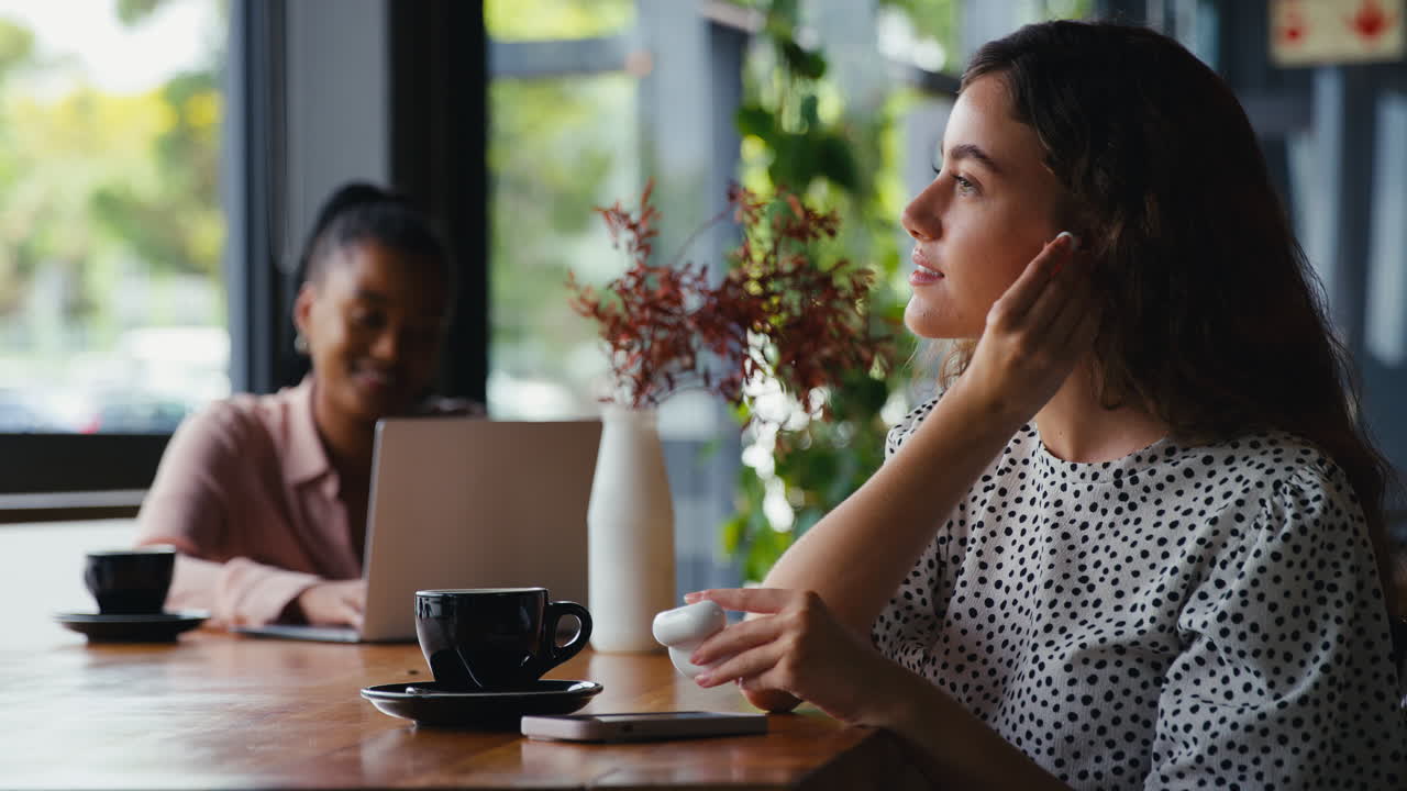 Geschäftsfrau mit Mobiltelefon setzt sich kabellose Ohrhörer ein und arbeitet im Café