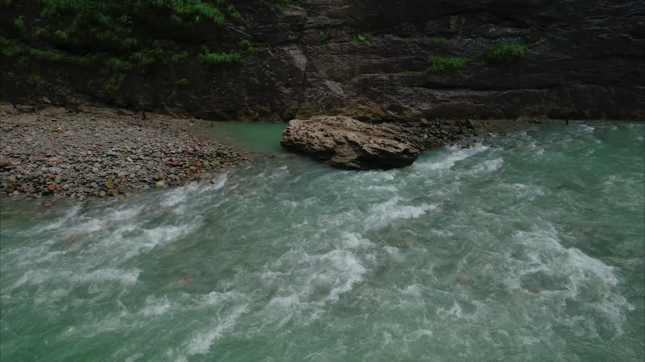 Pan shot of a turquoise mountain river flowing rapidly past a rocky shoreline