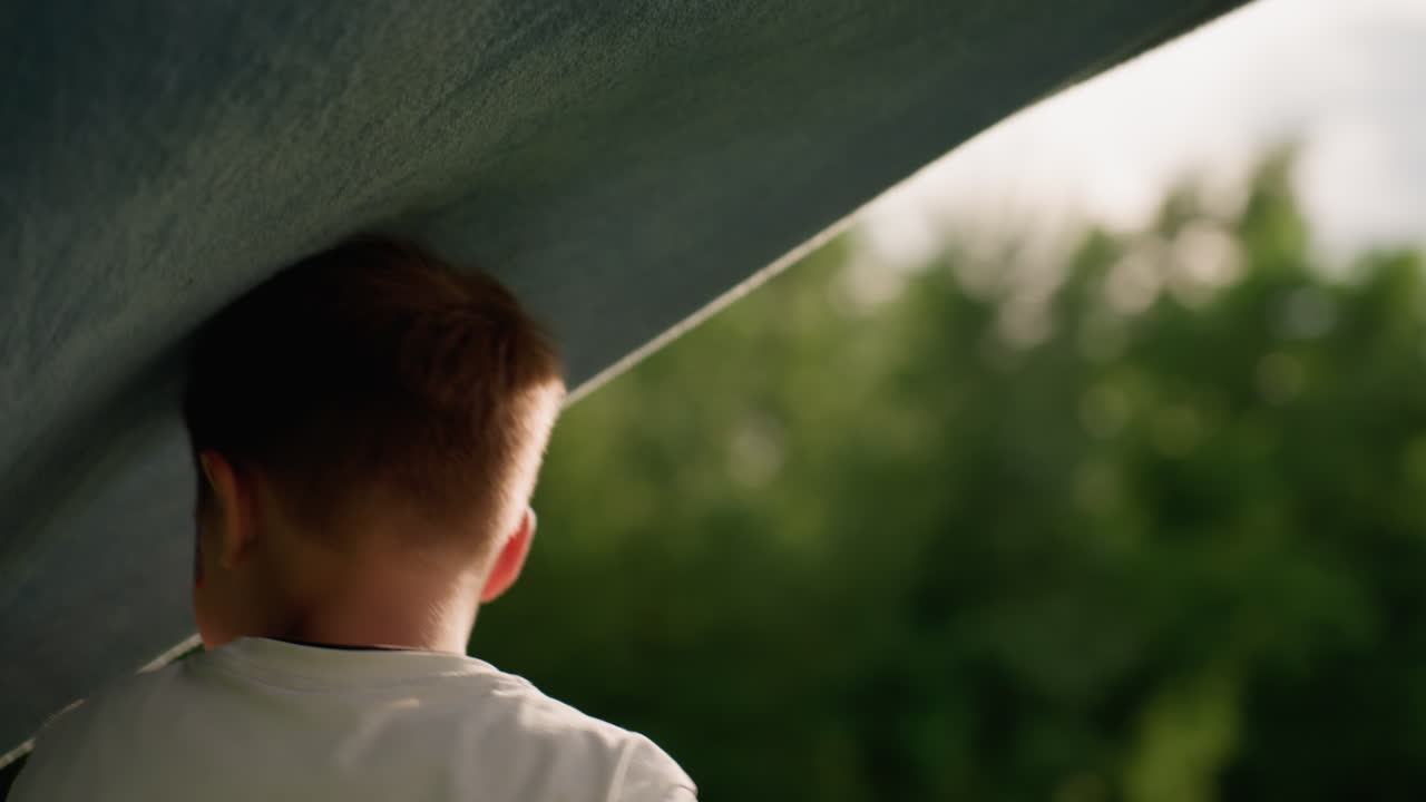 Summer kid playing with floating blanket, smiling and reaching up, warm sunlight on face, green park background, carefree movement showing joy and playful energy