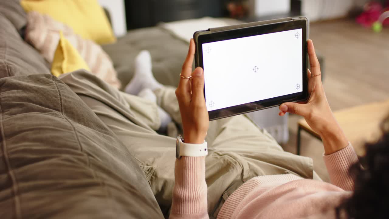 Nicht-binäre Person hebt Tablet an, um den Bildschirm zu kalibrieren und den Winkel auf der Wohnzimmercouch anzupassen.