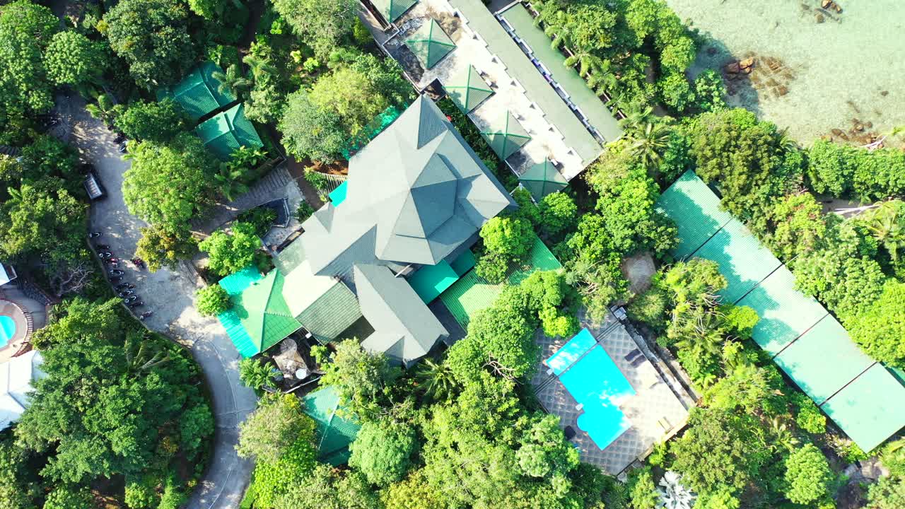 Colorful roofs of waterfront resort villas through green trees and beautiful gardens on shoreline of tropical island, Myanmar