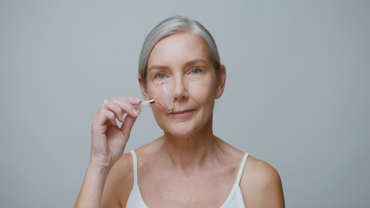 Mujer madura usando rodillo de jade para el cuidado facial