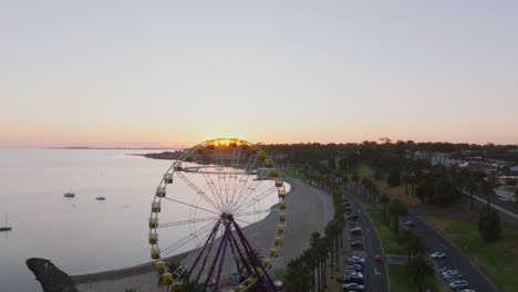 AERIAL-Morning-Sunlight-Peaking-Over-Horizon-and-Ferris-Wheel,-Australia