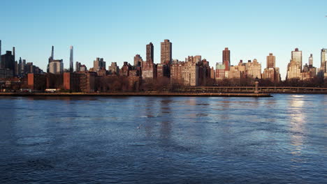 Aerial-view-low-over-the-East-river-and-the-cityscape-of-Yorkville,-New-York,-USA---tracking,-drone-shot