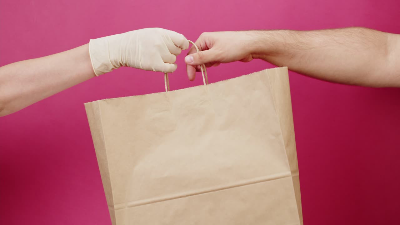Gloved Hand Delivering Paper Bag to Another Hand