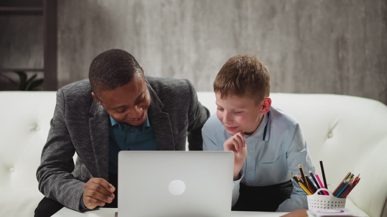 Gutt ser på video via laptop og ler med engelsklæreren.
