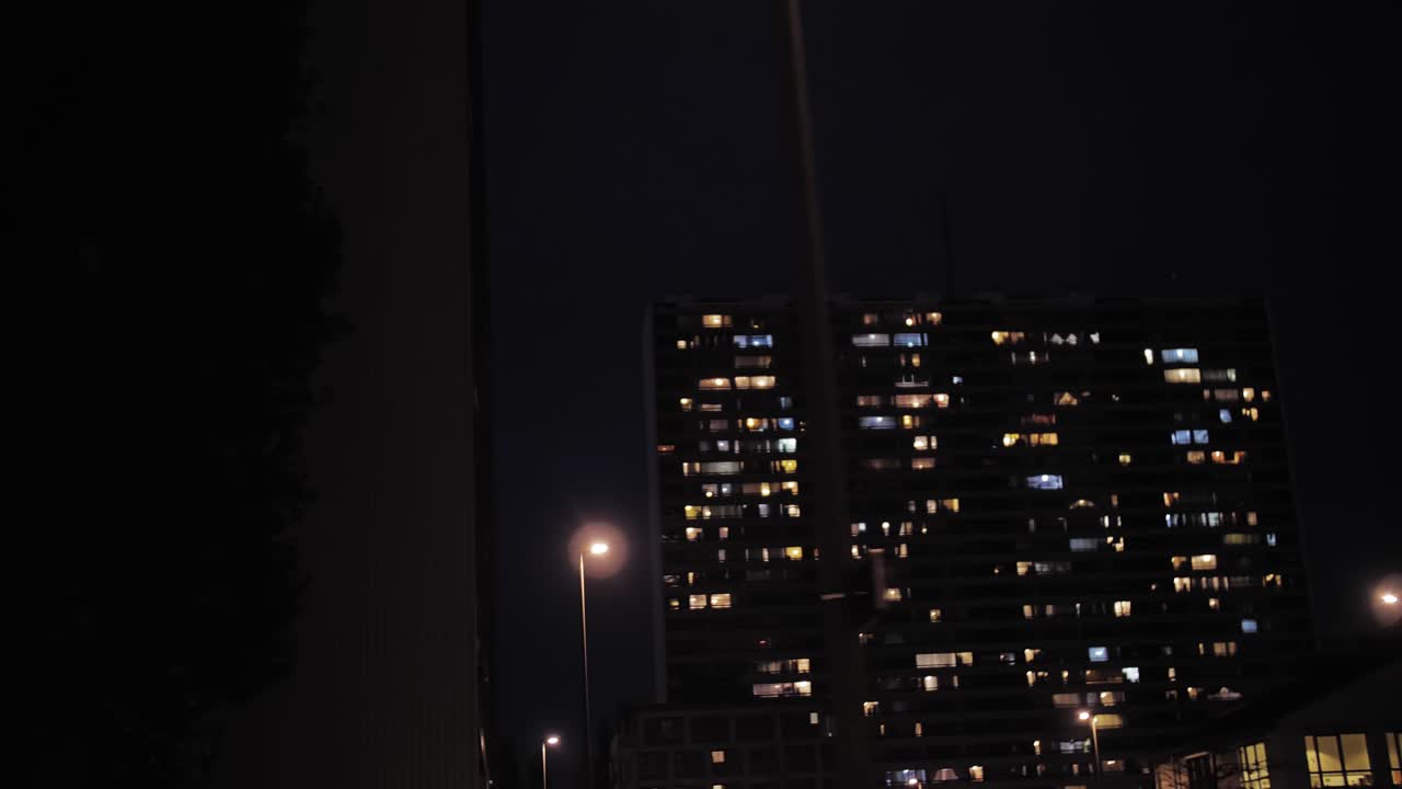 Passing urban high-rise buildings at night with scattered window lights and street lamps