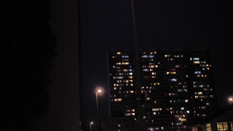 passing urban high-rise buildings at night with scattered window lights and street lamps