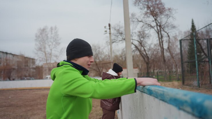 white trainer vaults small fence to retrieve ball while child watches, urban courtyard scene, gripping railing, momentum and careful landing, playful rescue of ball during chilly practice