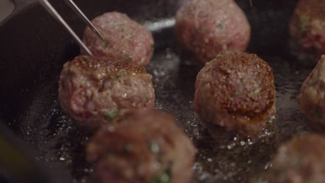 chef turns fried meatballs inside hot frying pan with boiling cooking oil