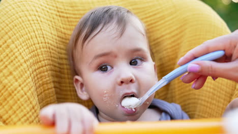 grey-eyed beautiful child nutrition. close up. mom's hand gives a spoon to her kid and he takes food.