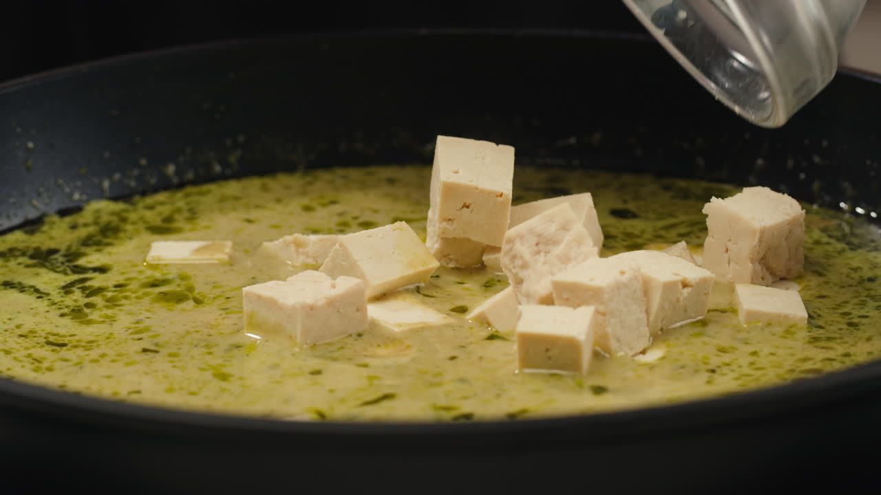 Tofu being added to a pan of sauce