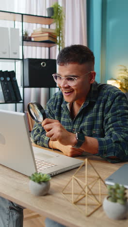 Business-man-working-at-home-office-holding-magnifying-glass-looking-at-laptop-screen-wow-expression