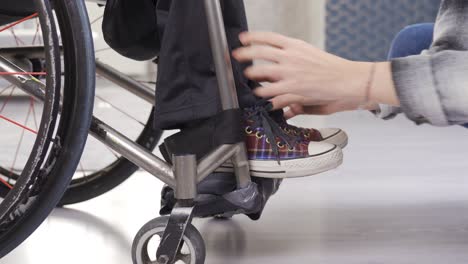 woman helps paralyzed legs of a disabled person sitting in a wheelchair.