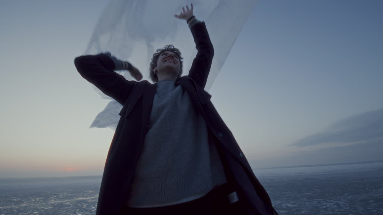 Loving Couple Playing with Fabric and Hugging by Frozen Lake at Sunset