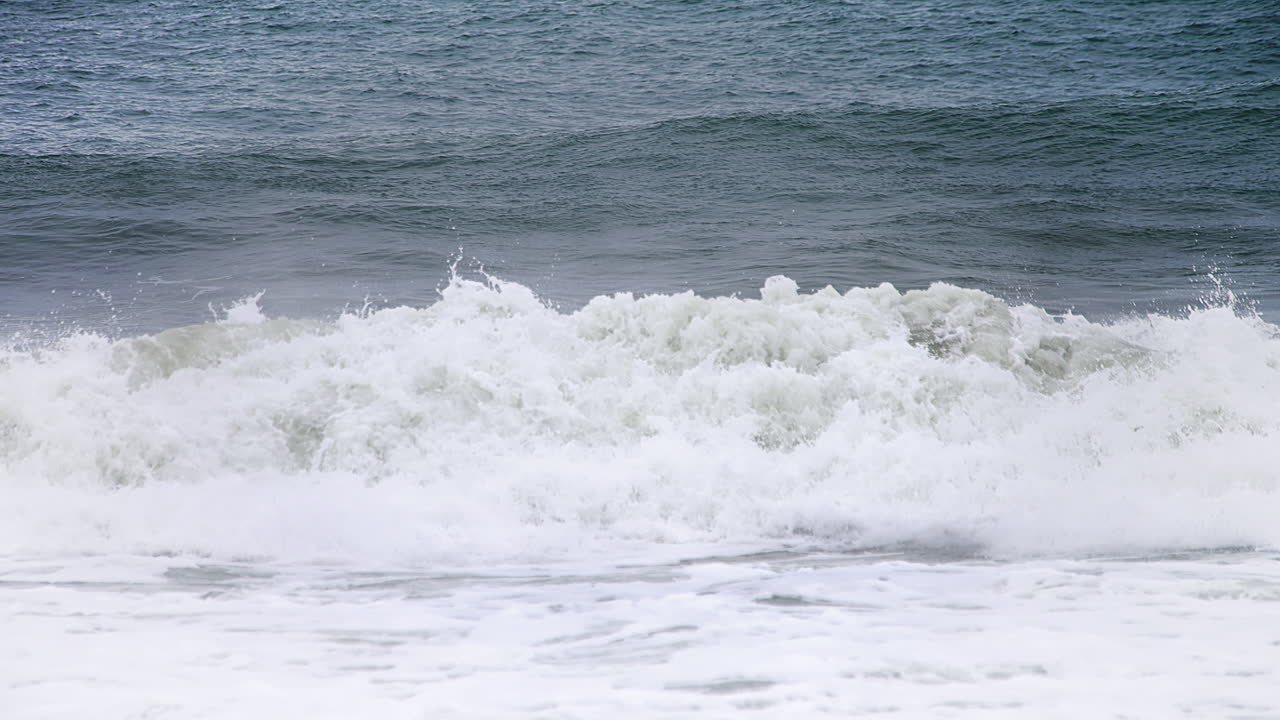 120fps 4k 푸티지에서 고속 카메라 120fps 4k 푸티지 뒤에 짙은 파란색 바다가 있고 흰색 물이 쏟아지는 해안에서 느린 동작으로 작은 충돌 파도에서 흰색 물 팬