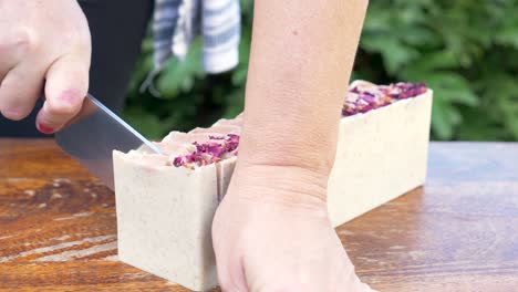 a women gently slices a newly made block of handmade soap with a sharp knife