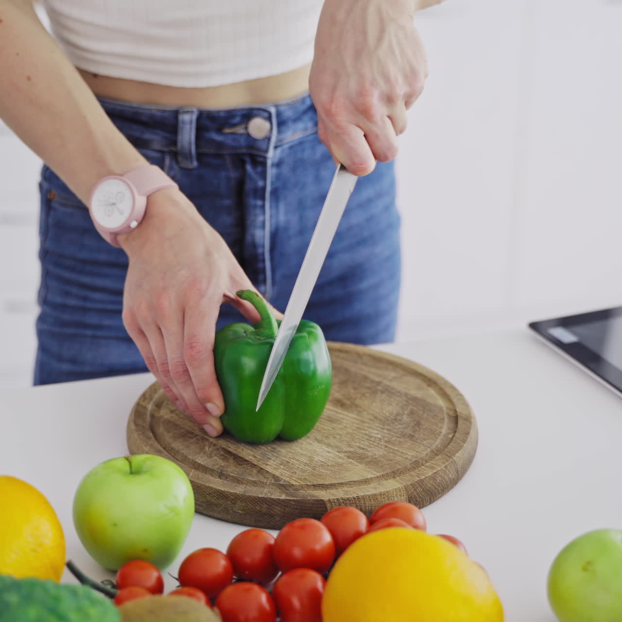 Young female is cutting green pepper on a wooden board. Close-up woman hands preparing healthy food on the kitchen on fresh ingredients background.