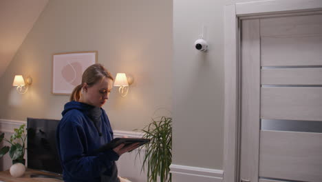 woman checking security camera on tablet in home