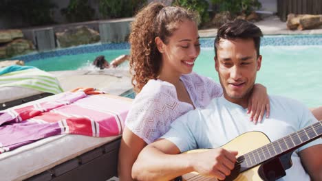 una pareja feliz y diversa enamorada abrazándose y tocando la guitarra en una fiesta en la piscina