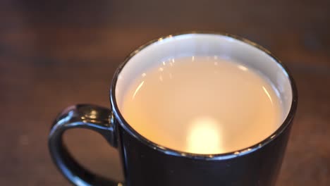 clip taken at coffee shop cafe of a black and brown coffee cup with hot coffee or tea in it, and reflection of light in liquid