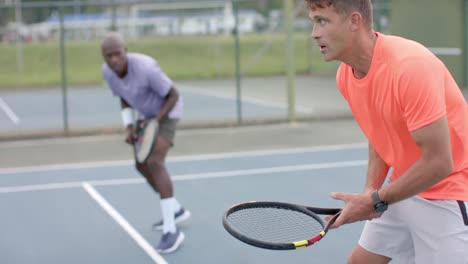 two diverse male friends playing doubles waiting for ball on outdoor court in slow motion