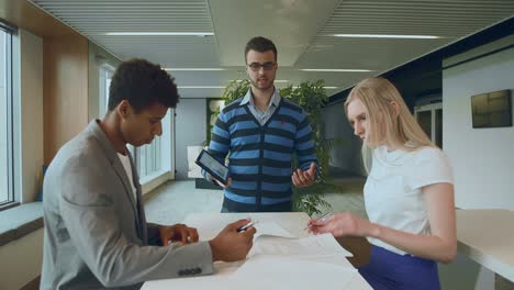 compañeros de trabajo multiétnicos con papeles y tableta. vista lateral de un hombre negro con compañeros de trabajo en la mesa leyendo papeles y usando tableta en equipo en la mesa