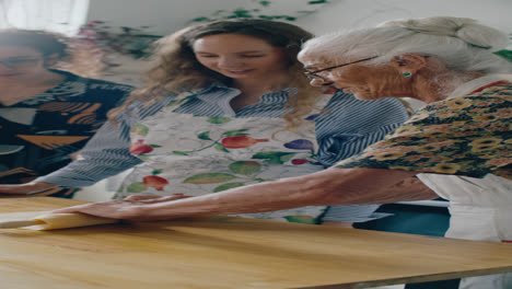elderly grandmother rolling dough as teaching family to bake pizza