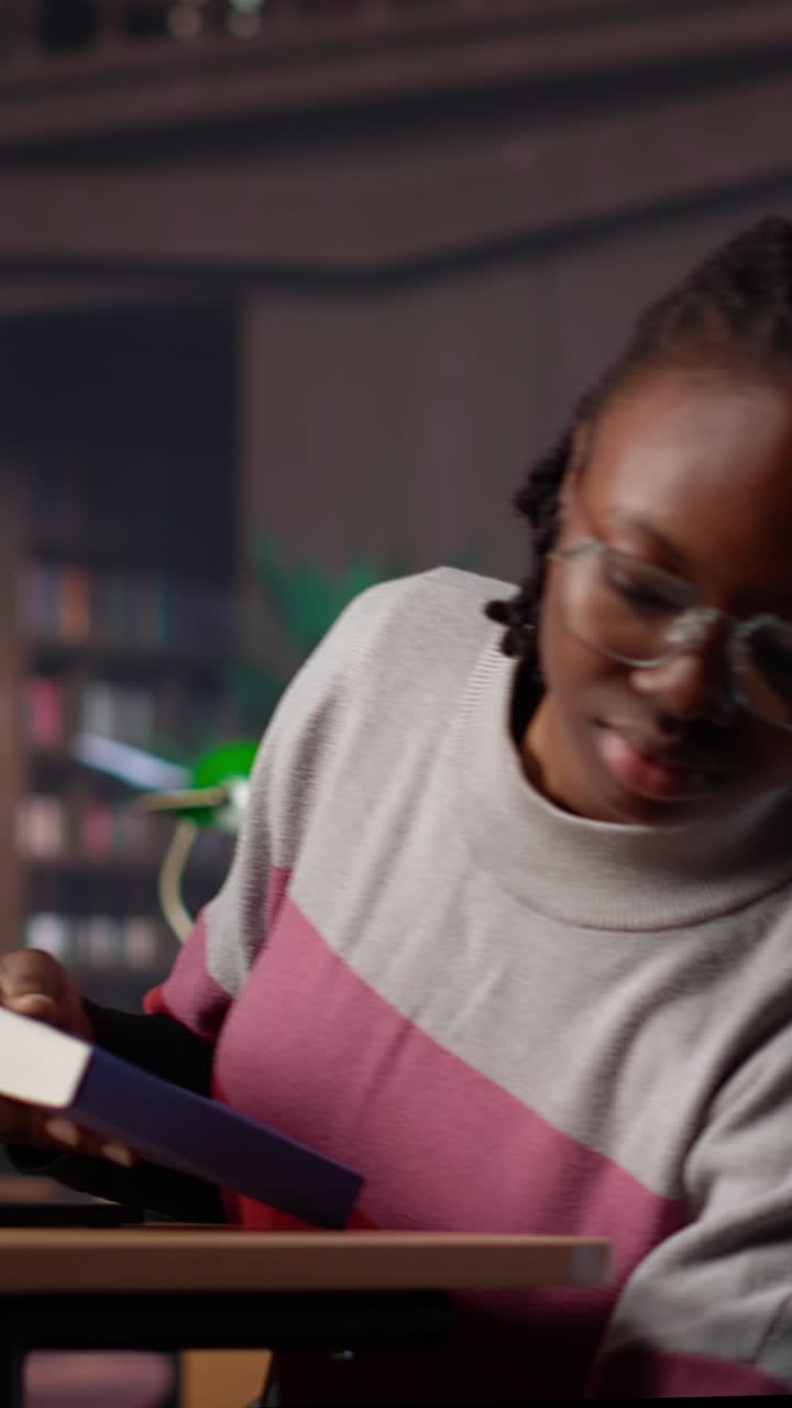 Vertical video african american student comparing class notes with data from the library