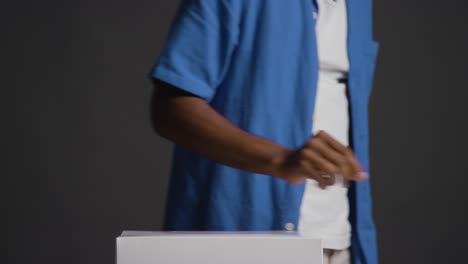 close up of man casting vote into election ballot box against black background