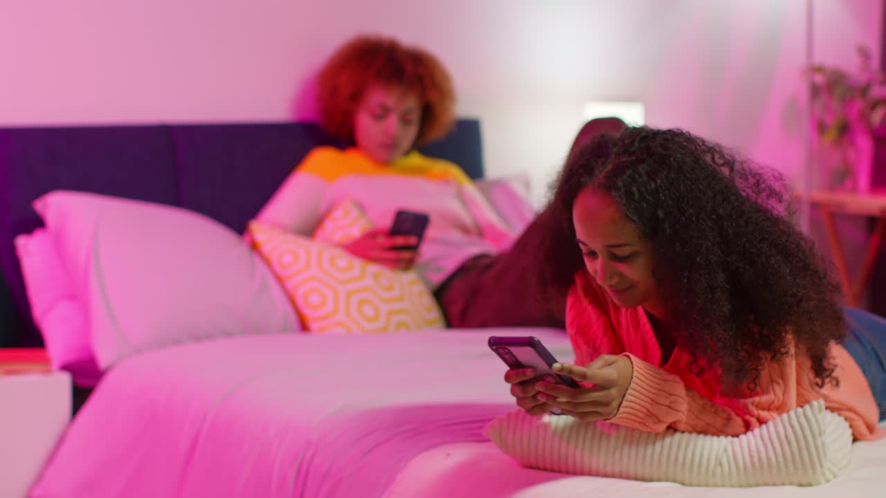 Two Friends Relaxing on Bed with Smartphones