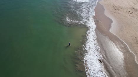 video aéreo de un dron de arriba hacia abajo de un pescador pescando en la playa de jimbaran en bali, denpasar, indonesia durante un día soleado con olas calmantes