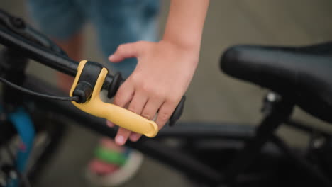 a close-up of a child's hand gripping the brake of a bicycle, the focus is on the child's hand and the yellow brake lever, while the background remains blurred