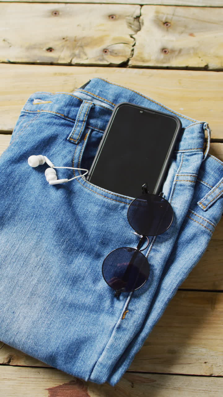 Vertical video of denim trousers with sunglasses, smartphone and earphones with copy space