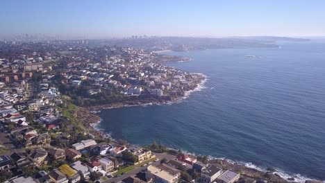 Vuelo-Aéreo-Sobre-La-Propiedad-Costera-Frente-A-La-Playa,-Casas-Oceánicas-Con-Vista-A-La-Ciudad-En-El-Horizonte-De-Fondo-En-Sydney,-Australia