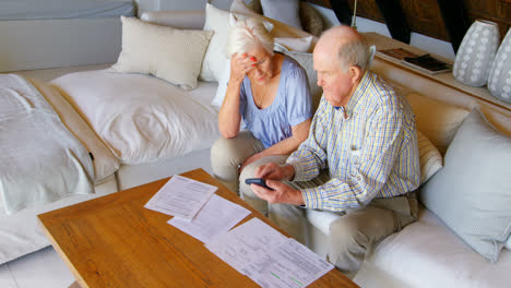 High-angle-view-of-old-Caucasian-senior-couple-discussing-over-bills-in-living-room-at-comfortable-h