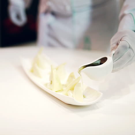 professional chief-cooker pouring special sauce on pieces of cheese laid out well on the plate. beautiful presentation of appetiser.