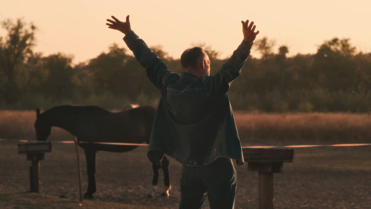 Man with arms raised at sunset by horses