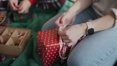 woman tying ribbon on wrapped christmas gift at home