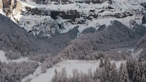 Una-Vista-Aérea-Del-Circo-Du-Fer-à-Cheval-Mientras-Está-Cubierto-De-Nieve-Durante-Un-Frío-Invierno,-Volando-Hacia-Atrás-E-Inclinándose-Hacia-Arriba-Para-Revelar-La-Impresionante-Cara-Del-Circo-Que-Se-Yergue-Ante-El-Valle-Helado