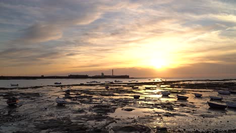 Stunning-sunset-at-ocean-during-low-tide-and-fishing-boat-silhouettes