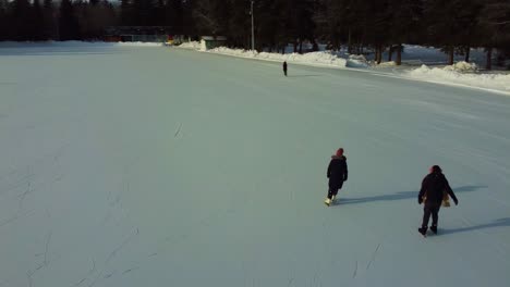 4k aerial flyover from behind couples double dating at manmade ice skating rink surrounded by tall park trees next to a valley golf course snow covered by residential towers condos overlooking them