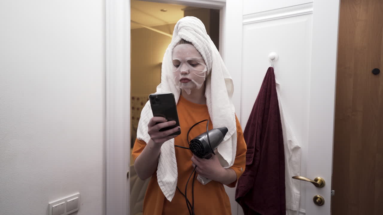 Woman in bathroom getting ready with face mask and hair dryer