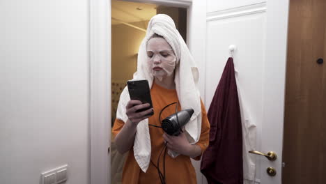 woman in bathroom getting ready with face mask and hair dryer
