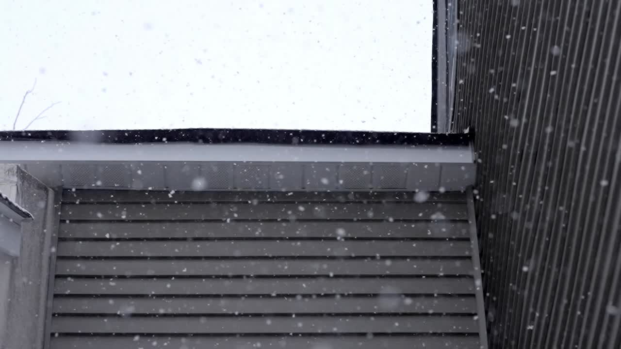 Slow falling snowflakes on a roof of a house on a cold winter day, cloudy sky, snowfall, static shot, copy space