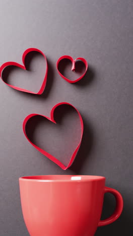 video vertical de taza roja y corazones rojos flotantes, en fondo gris con espacio de copia